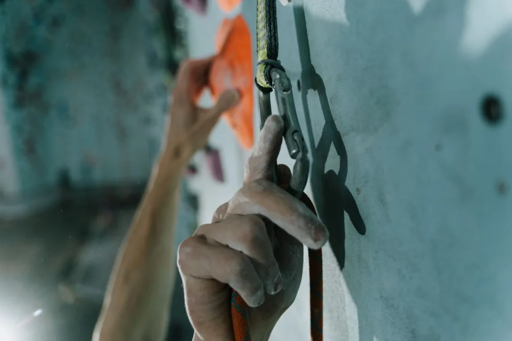 Mão conectando um mosquetão à corda de escalada